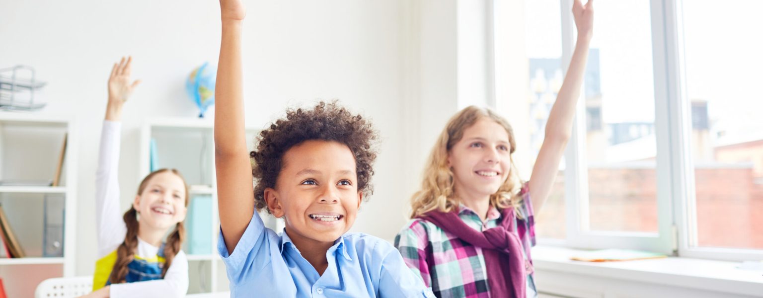 Happy and clever learners of elementary school raising their hands at lesson